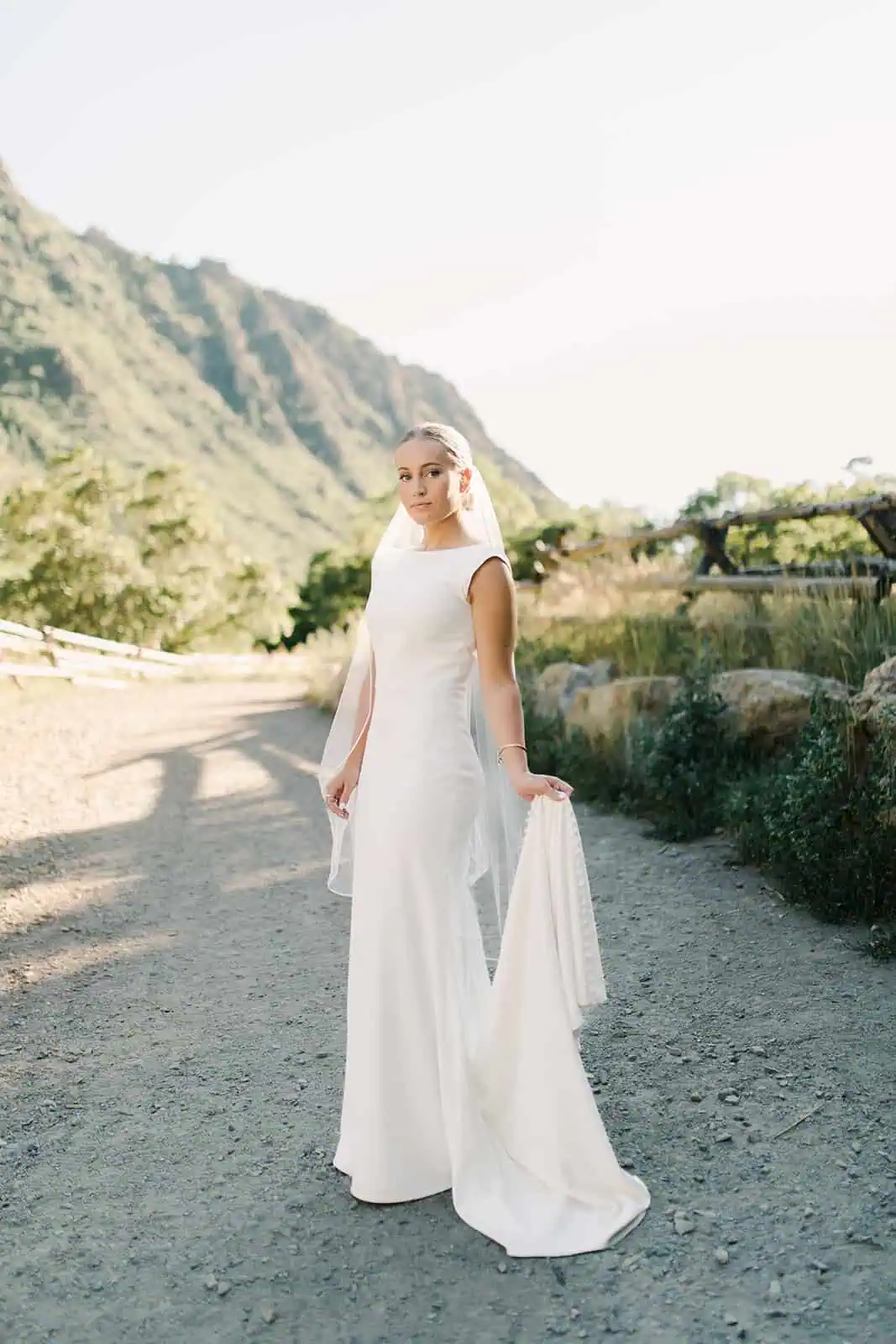 Bridal portrait of a woman in a white wedding gown outdoors with mountains and greenery in the backg.