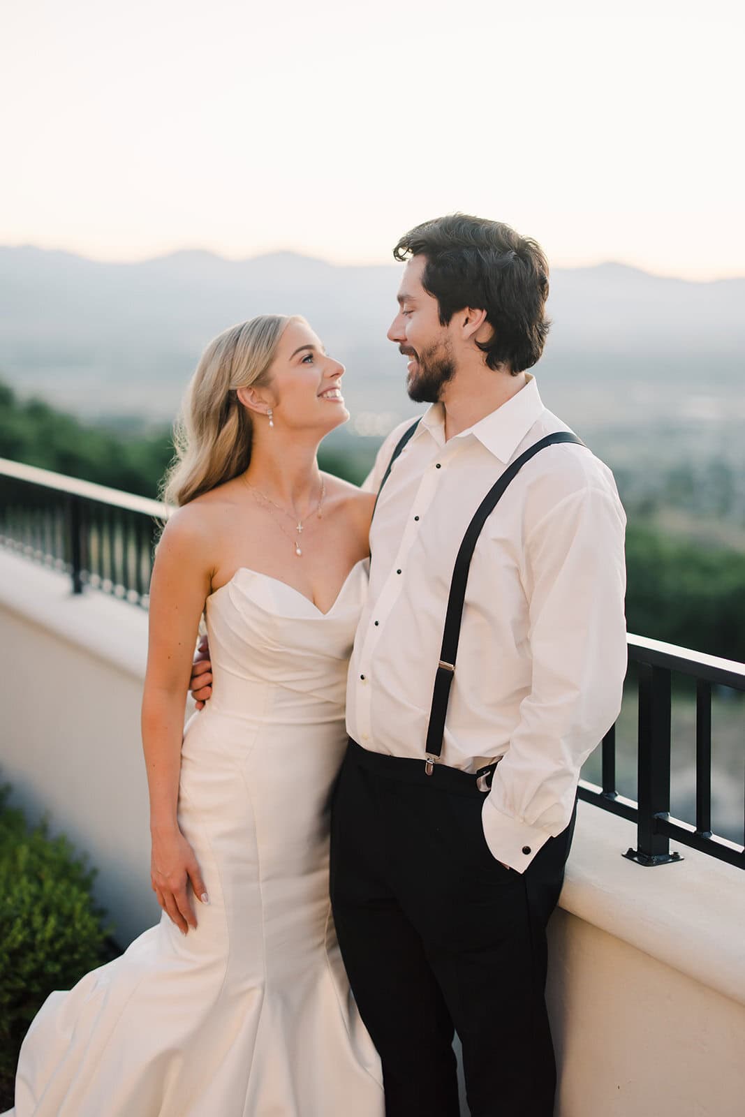 Wedding couple smiling on balcony overlooking scenic landscape.