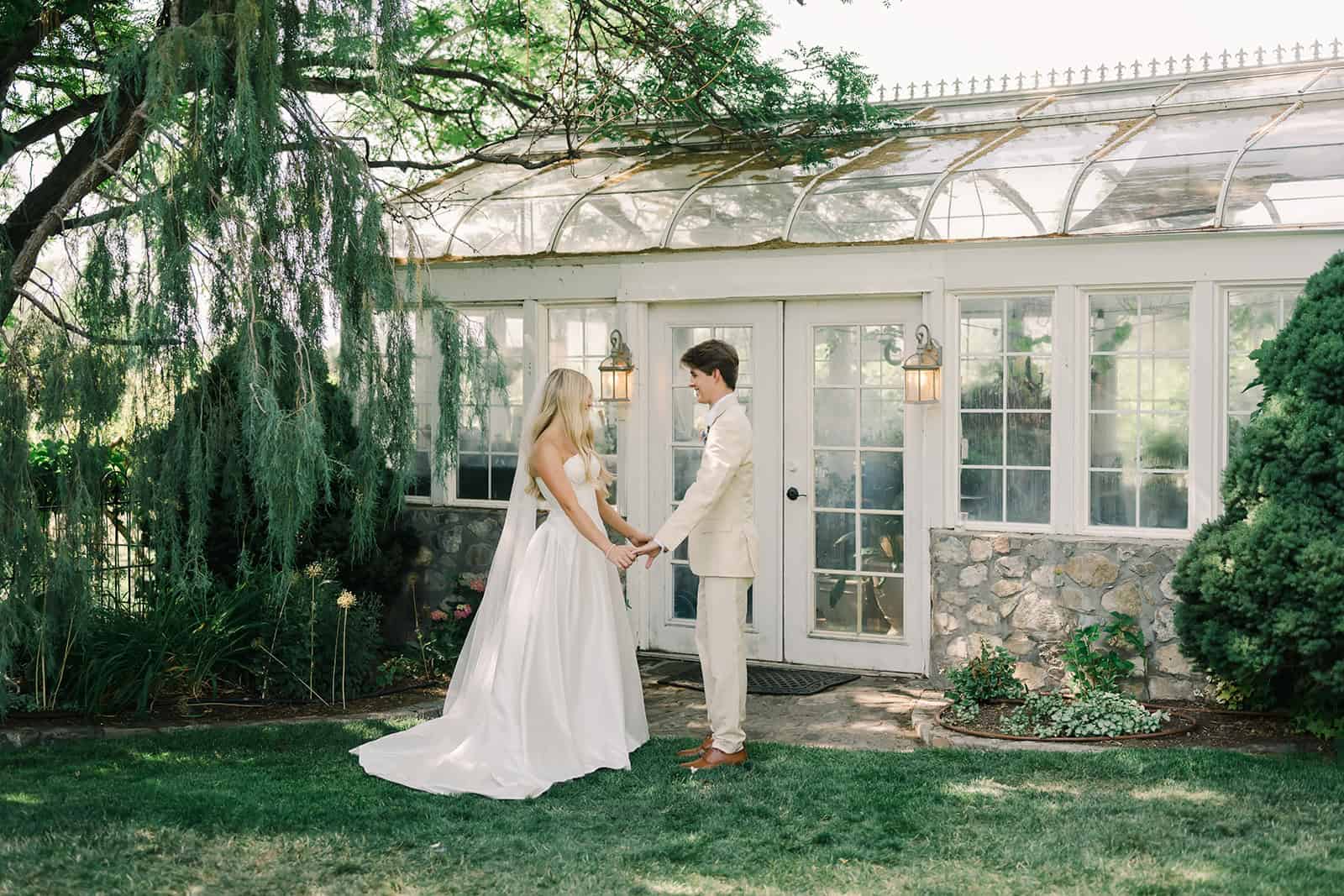 Wedding couple holding hands outside greenhouse in a lush garden setting.