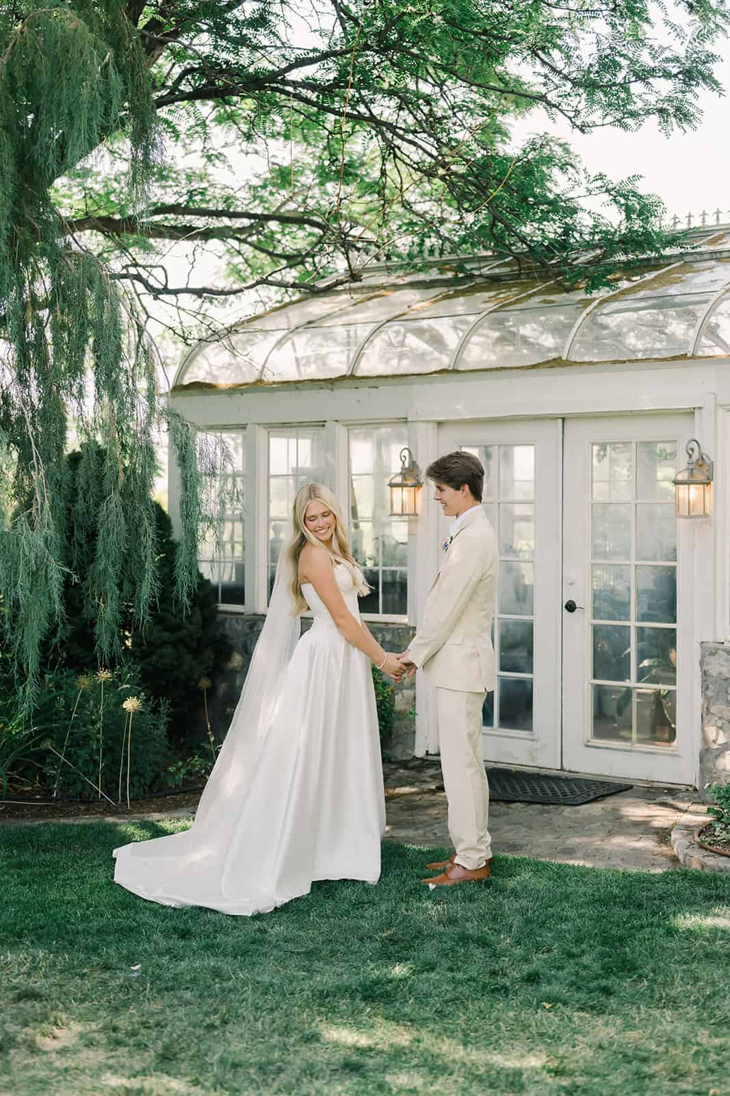 Wedding couple holding hands in front of greenhouse during daytime.