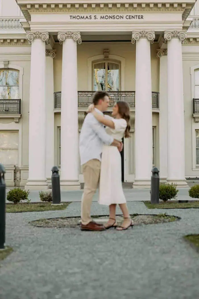 Couple embracing in front of Thomas S. Monson Center, a historic building with classical architectur.